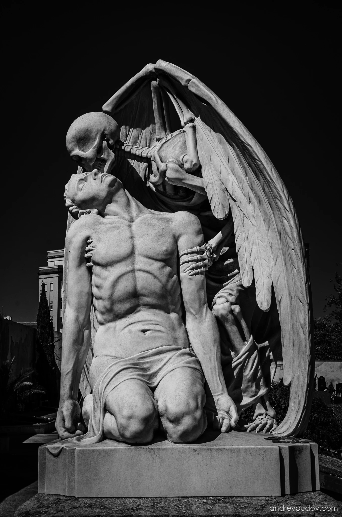 Favorite Photographs - The Kiss of Death

The Kiss of Death is a marble sculpture, found in Poblenou Cemetery. The sculpture is thought to have been created by Jaume Barba, although others have claimed that its idea was conceived by Joan Fontbernat. The sculpture depicts death, in the form of a winged skeleton, planting a kiss on the forehead of a young man. The sculpture elicits varying responses from viewers concerning the depiction of the young man ranging from ecstasy to resignation.

"His young heart is thus extinguished. The blood in his veins grows cold. And all strength has gone. Faith has been extolled by his fall into the arms of death. Amen."